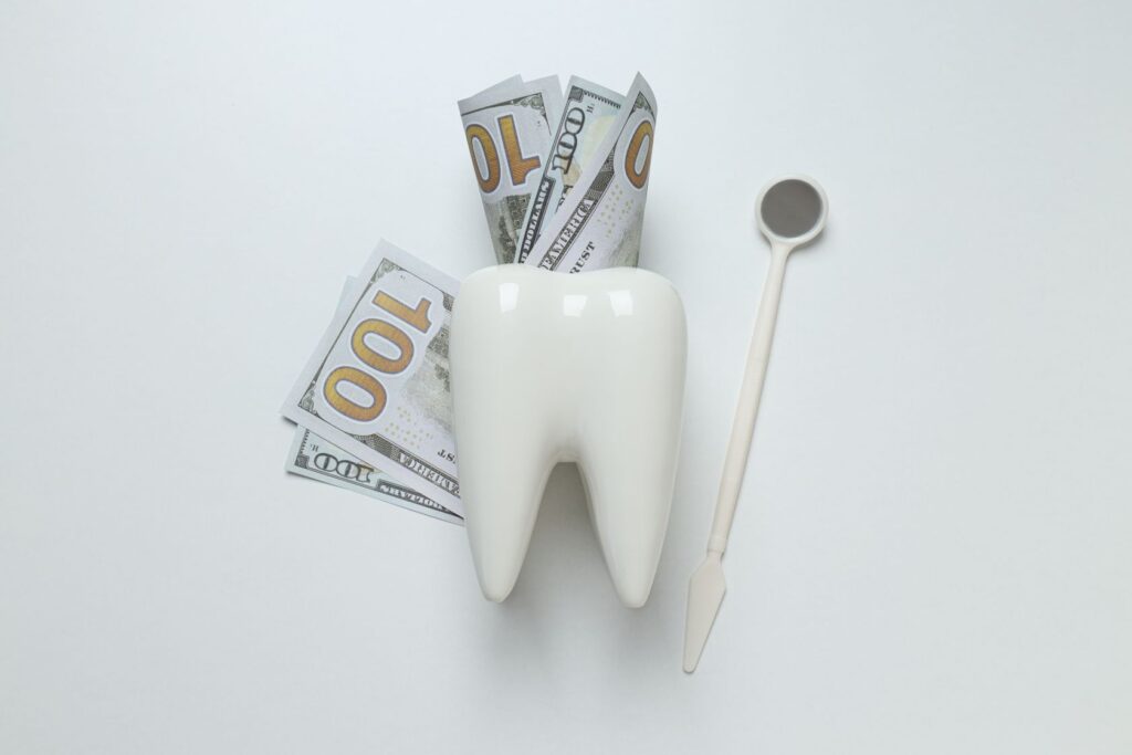 Tooth model with dollar bills and dental mirror representing porcelain veneers cost