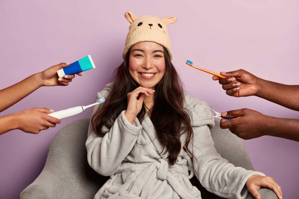 Smiling woman in a bathrobe surrounded by toothbrushes and toothpaste, illustrating easy at-home care after dental veneers.