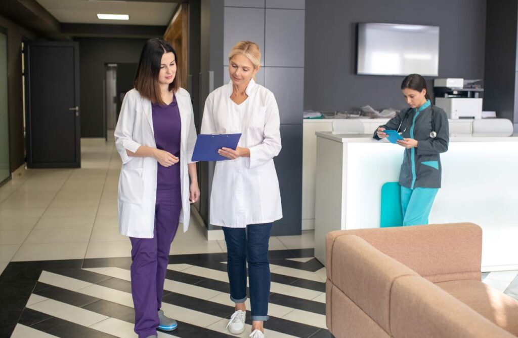 Dental team walking through a modern clinic reception, reviewing a clipboard while a nurse works at the front desk.