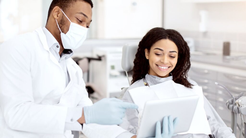 Dentist discussing a smile makeover plan with a patient in a modern dental clinic, using a tablet during a cosmetic consultation.