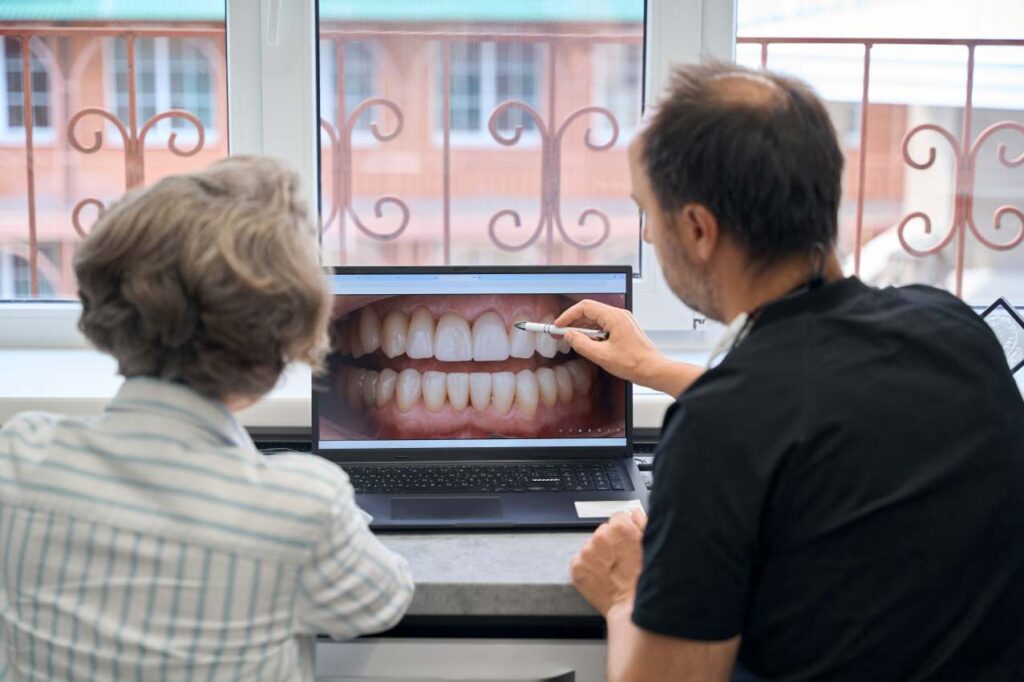 Dentist reviewing dental photos on a laptop with a patient during a bite check and smile planning