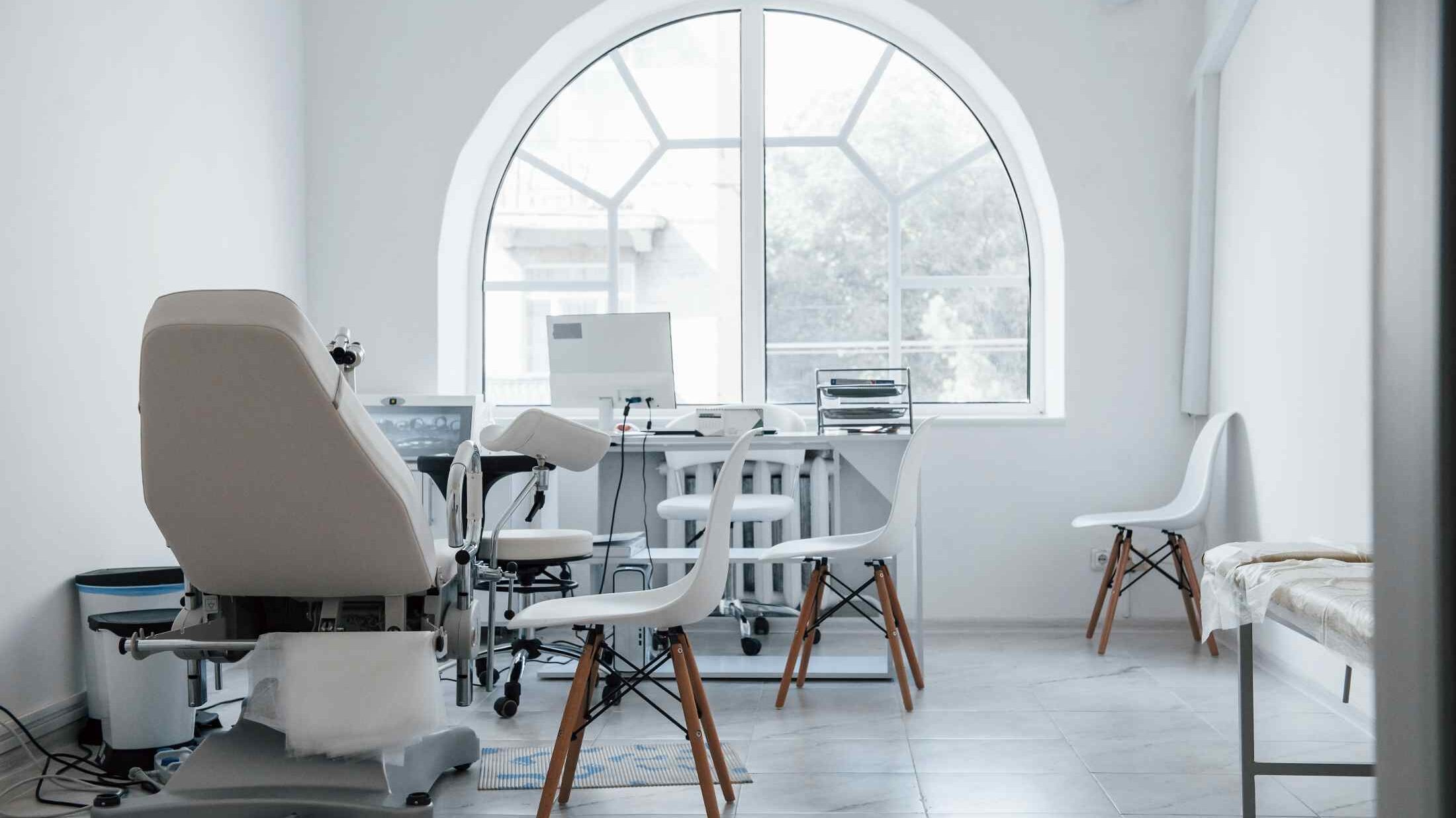 Modern dental clinic treatment room with a dental chair, patient seating, and large arched window, illustrating how location and clinic type can affect pricing.