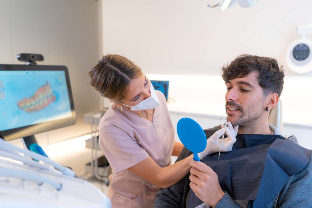 Dentist examining a patient holding a hand mirror during a consultation before Hollywood smile treatment in France.