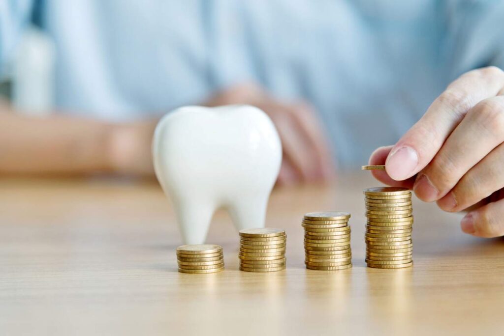 Person stacking coins beside a tooth model, showing why pricing can differ for a hollywood smile in italy.
