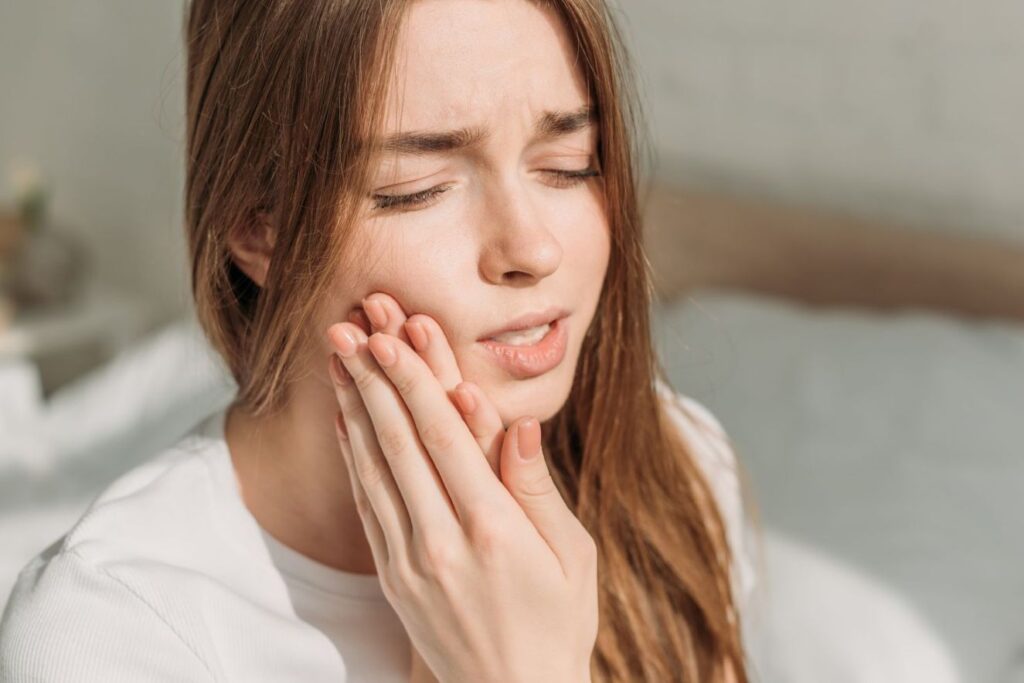 Woman holding her cheek with tooth pain, showing possible sensitivity after Hollywood smile veneers in Mexico