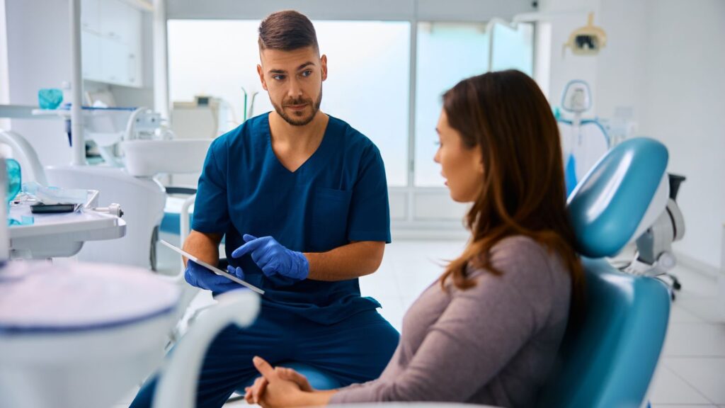 When should you see the dentist first? Dentist consulting with a patient in a dental chair before cosmetic treatment.