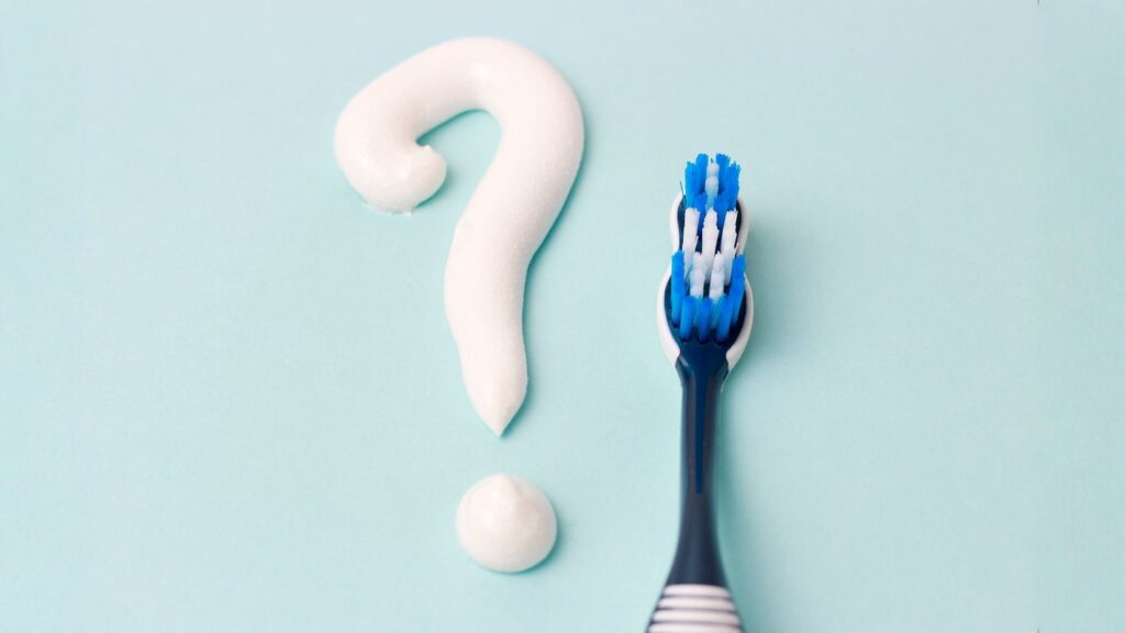 How to reduce Hollywood smile risks: a practical checklist, shown with a toothbrush and toothpaste shaped like a question mark on a light background.