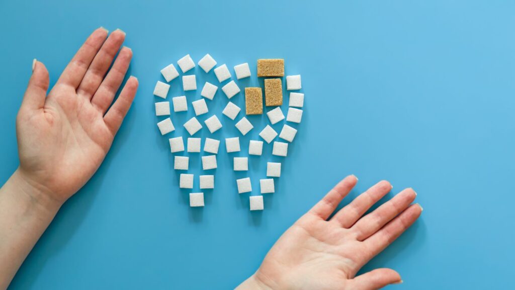 Hands framing a tooth shape made from sugar cubes on a blue background, illustrating dental health risks and trade-offs.