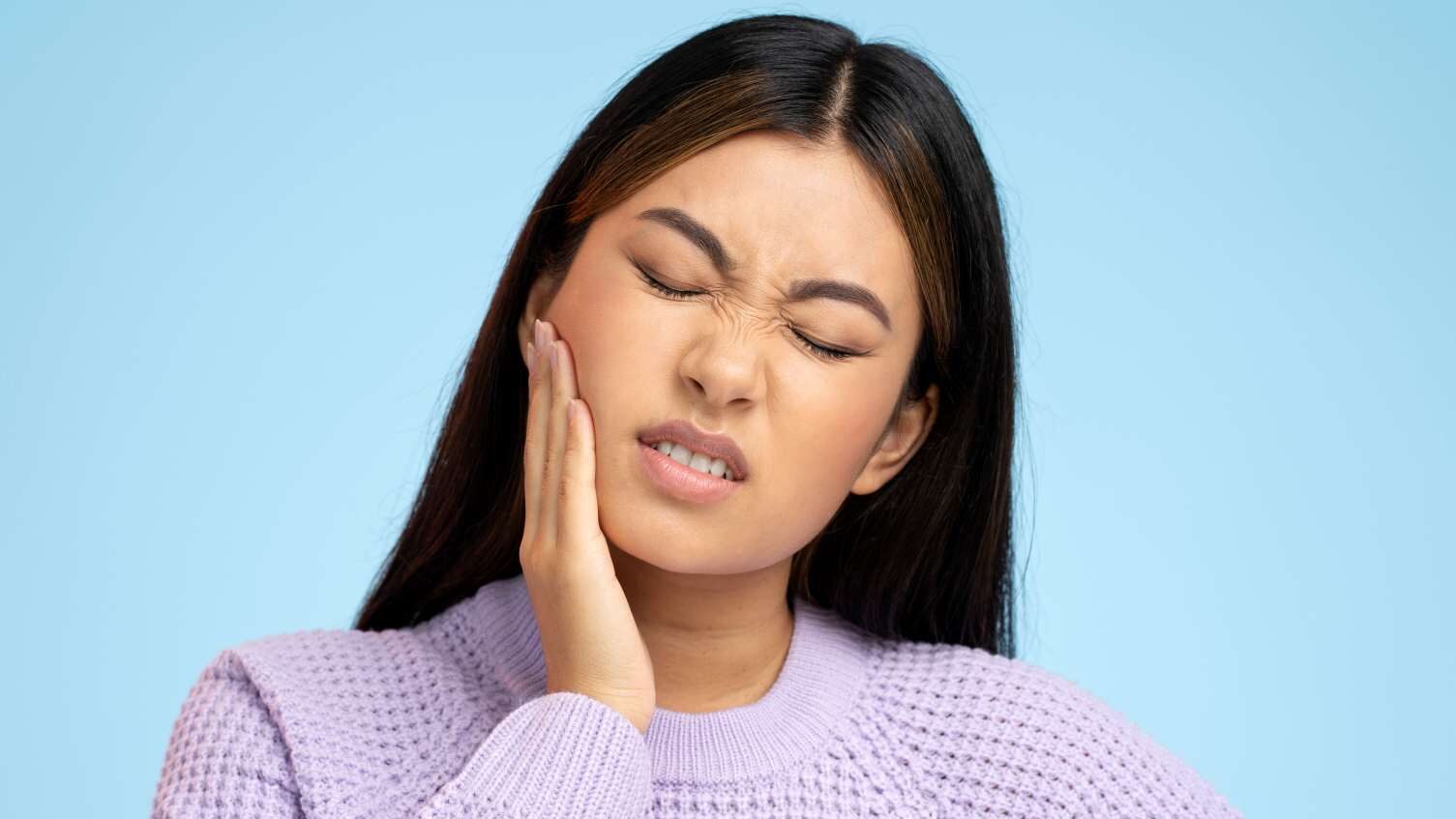 Woman holding her jaw with tooth pain, illustrating Hollywood smile risks like sensitivity and discomfort after cosmetic dentistry.
