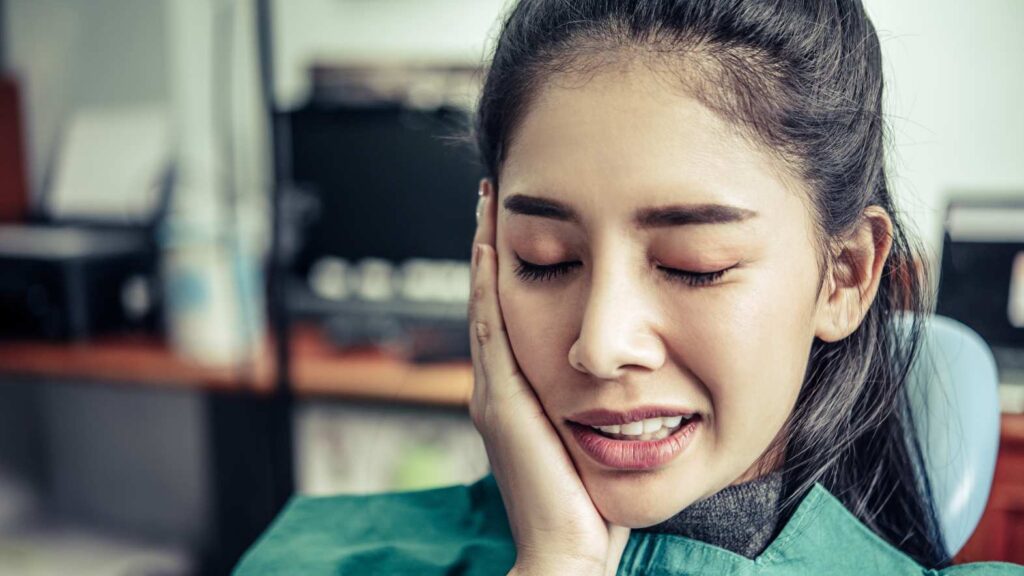 Risks & limitations showing a patient holding her cheek in pain, representing possible sensitivity or discomfort after cosmetic dental treatment.
