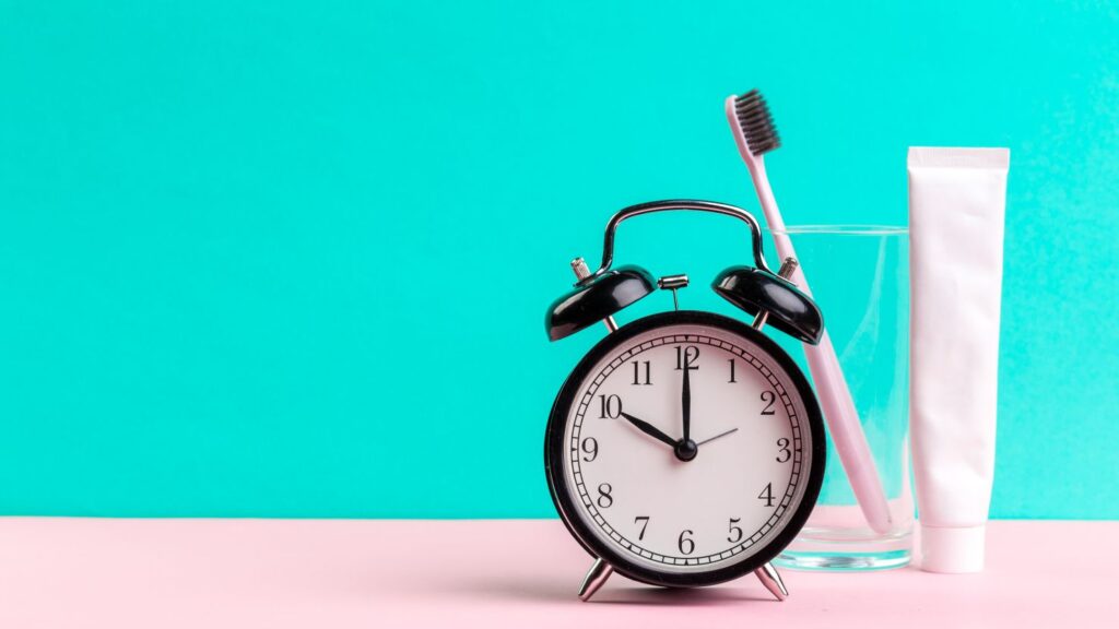 Alarm clock with toothbrush and toothpaste illustrating daily veneer care routine and brushing twice a day