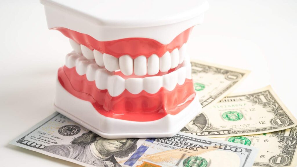 Dental model with white teeth sitting on U.S. dollar bills, illustrating the cost of a Hollywood smile in Egypt.