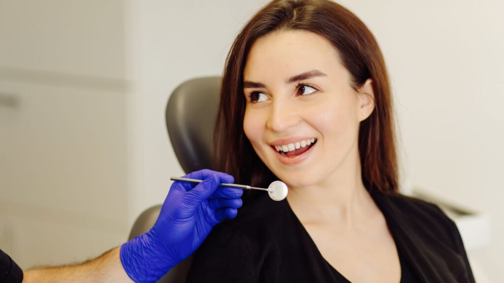 Dentist examining a woman's teeth with dental mirror during a routine dental checkup