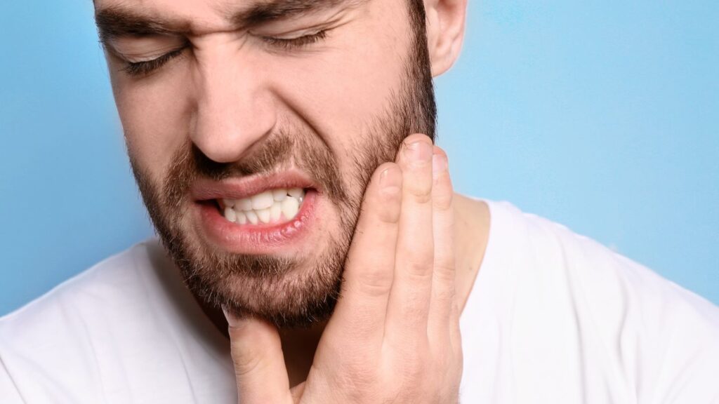 Close-up of a man holding his cheek in dental pain, representing cavities or tooth problems that should be treated before cosmetic dentistry.